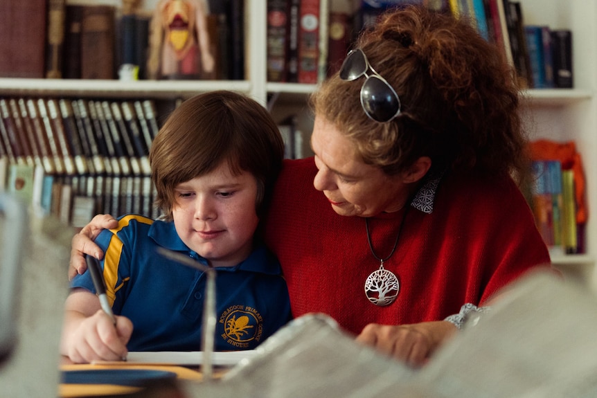 A woman sits and reads with her young son. The son is wearing a school uniform.