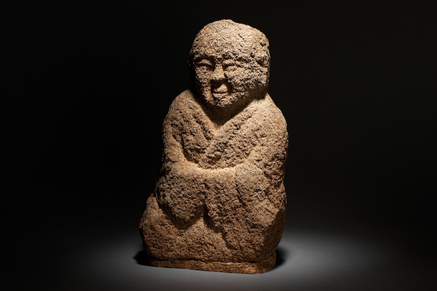 Small stone sculpture, figure of a robed man sitting cross-legged in Buddhist pose.
