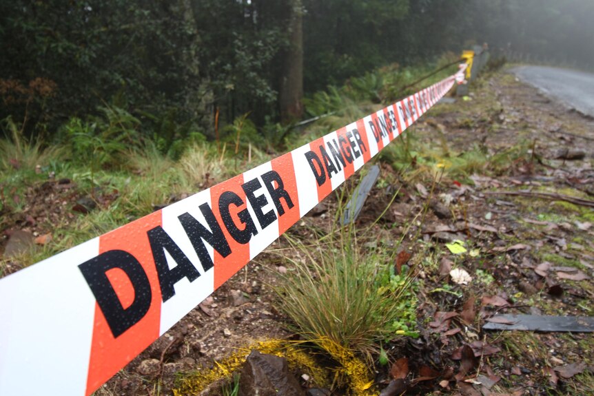 Tape across the crash scene on the side of a road with "danger" written on it.