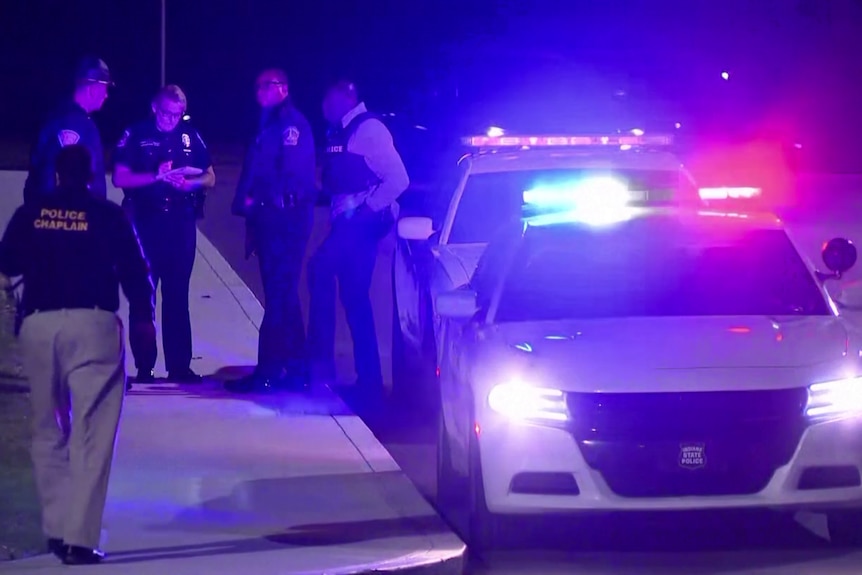 Police officers stand beside a vehicle displaying flashing lights.