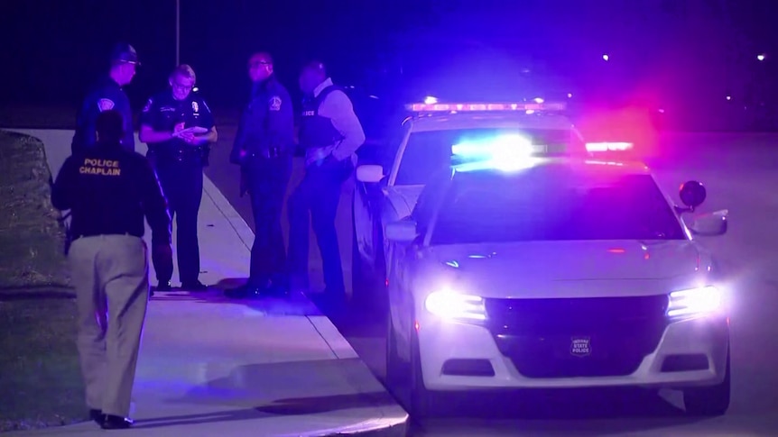 Police officers stand beside a vehicle displaying flashing lights.