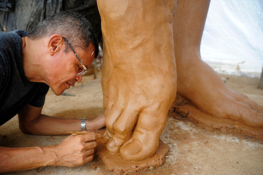 Artist Yino Marquez sculpting one of the toes of Shakira's statue. He is wearing glasses, has short black hair.