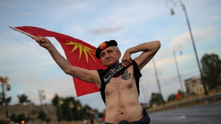 Man waving Macedonian flag lifts shirt to show tattoo