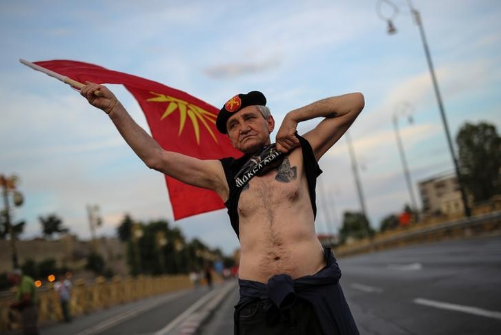 Man waving Macedonian flag lifts shirt to show tattoo
