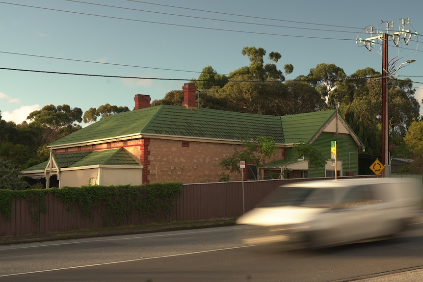 A house with a green roof with a blurred white car driving past