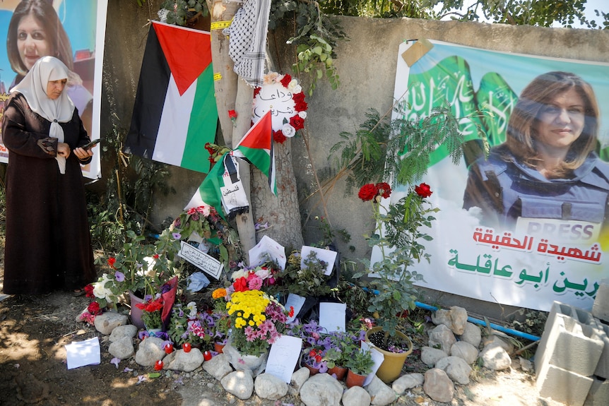 Woman stands beside vigil laid with flowers and posters of killed journalist.