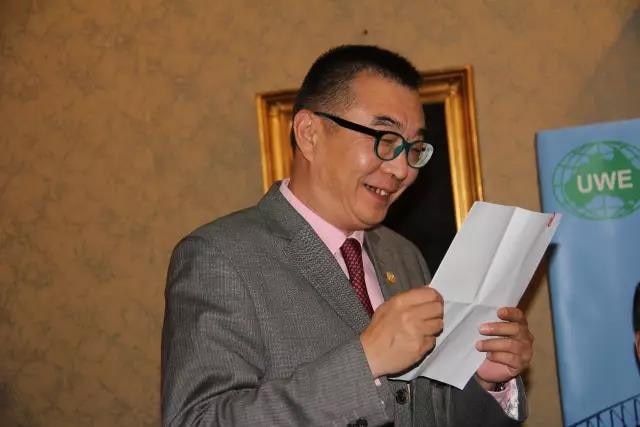 A be-suited Chinese man smiles as he looks at a document.