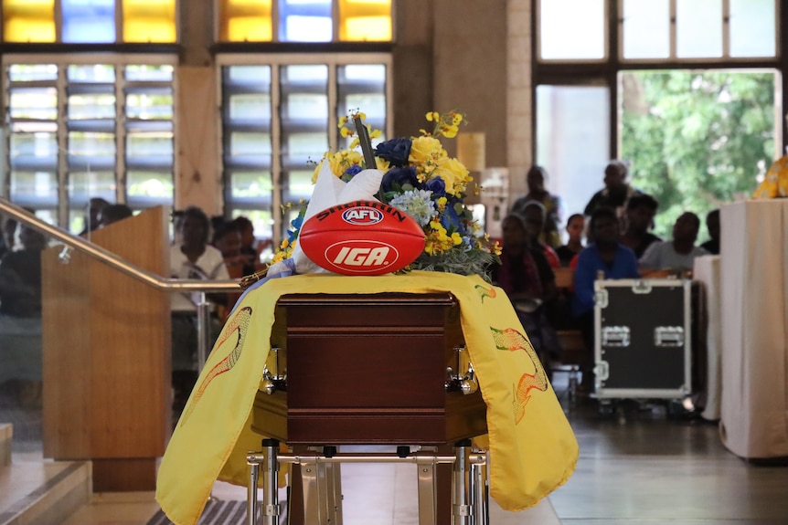 A red AFL ball sits on top of a casket in a church. 