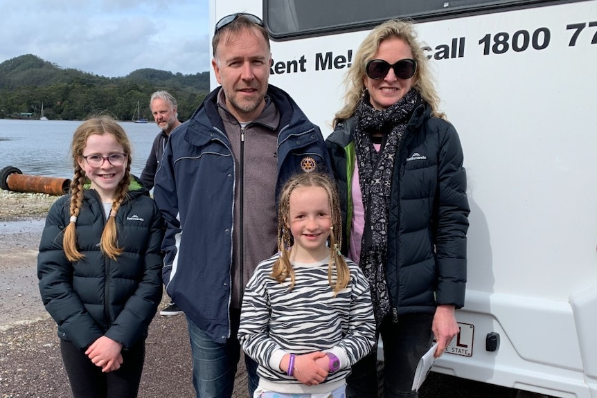 A man and his wife and two children stand in front of a hire van