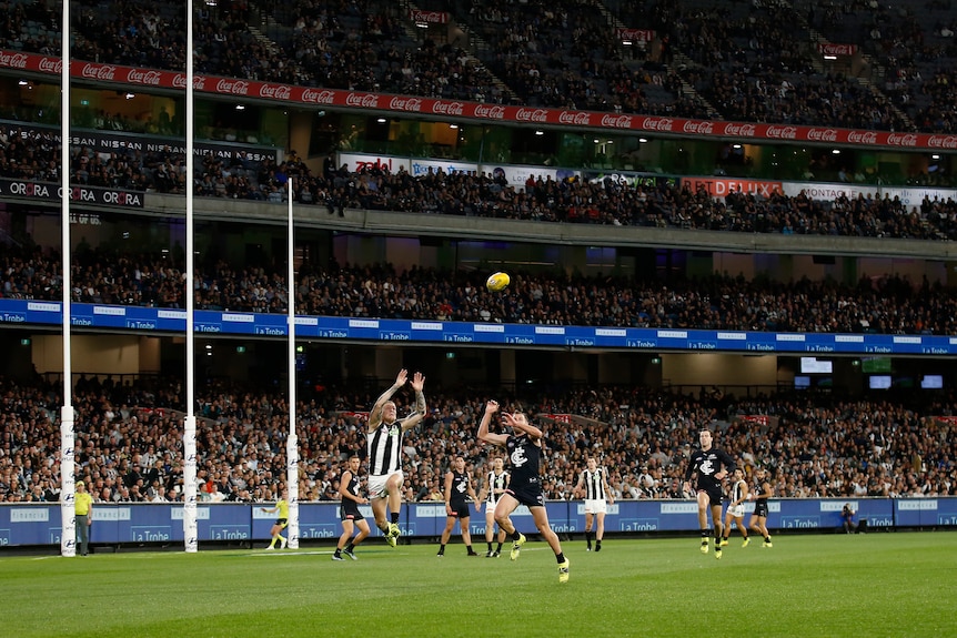 Lots of people back the MCG in the background as Jordan De Goey attempts to take a mark during an AFL game.