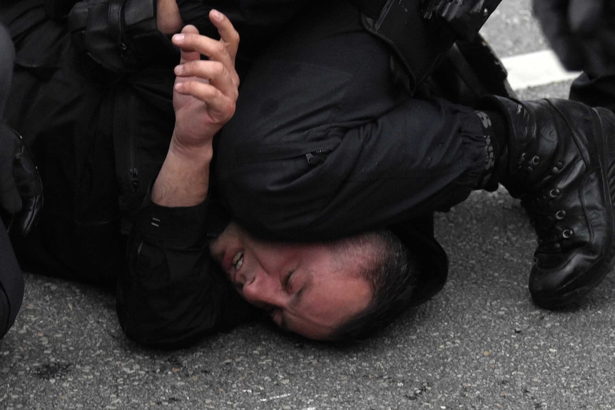 A policeman kneels on a mans head.