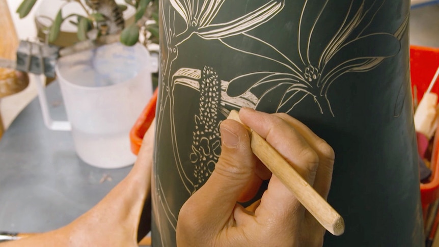 Hands are carving in a garden motif into a close-up view of vase
