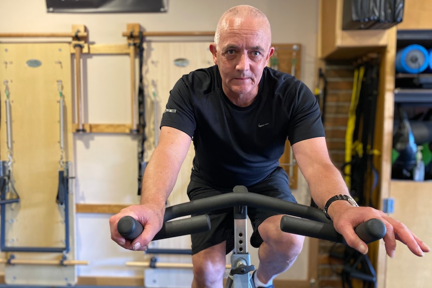 Glen Fearnett sits on an exercise bike and looks at the camera.