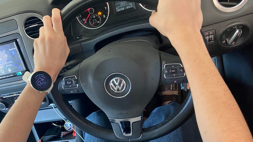 Hands on a steering wheel with a smart watch on the left wrist. 