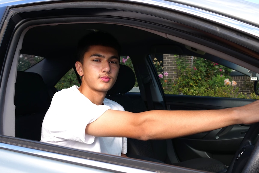 A man sitting in the driver's seat of car with his right hand on the wheel 