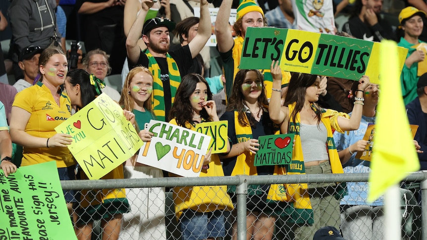 People hold up signs and wear green and gold