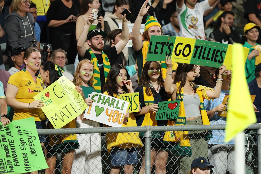 People hold up signs and wear green and gold