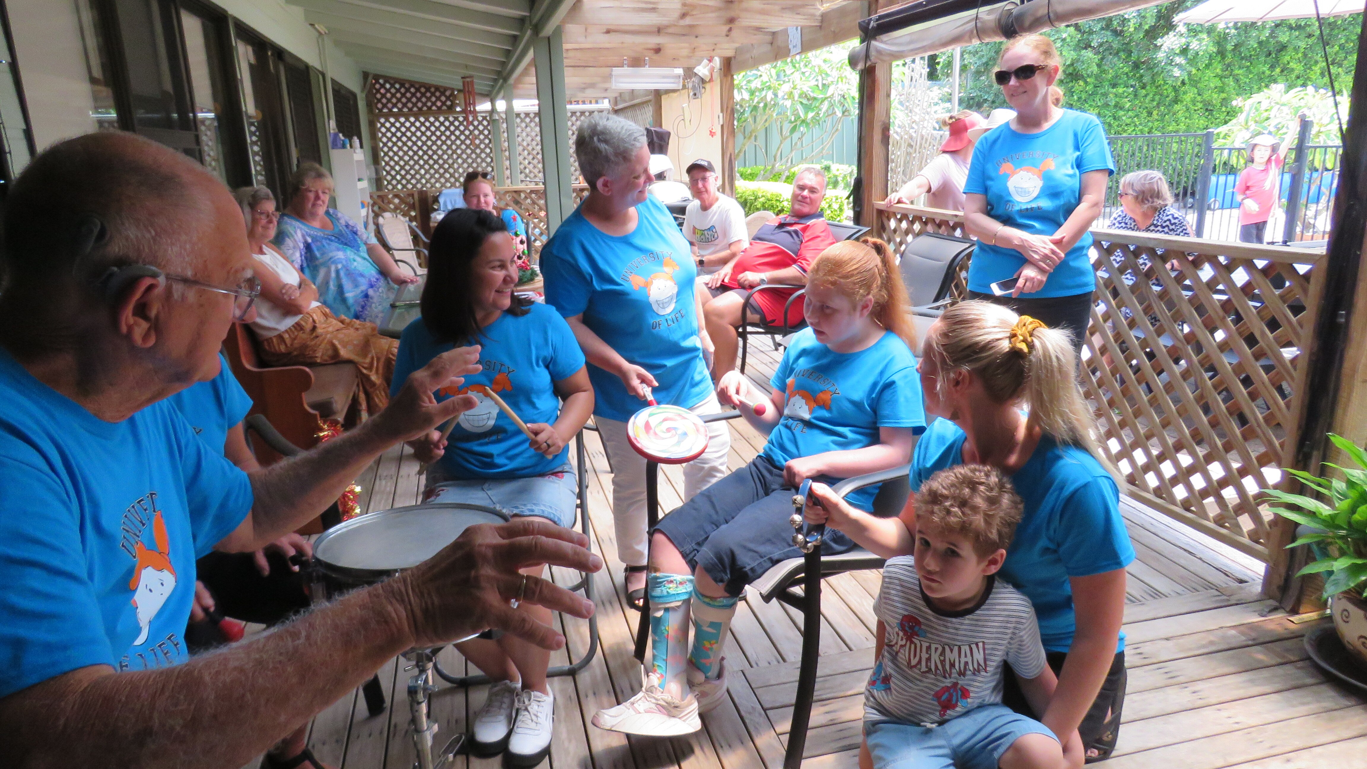 Many people sitting around Lillian wearing blue UOL T-shirts - Lillian, - red hair, holds a small frame drum and stick beater