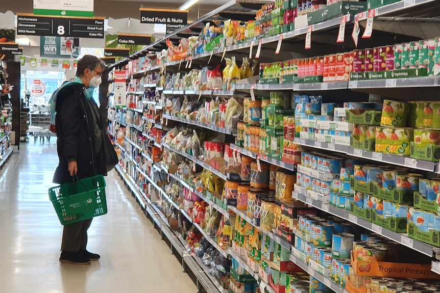 Woman in mask shopping in Woolworths packaged food aisle June 28, 2022.