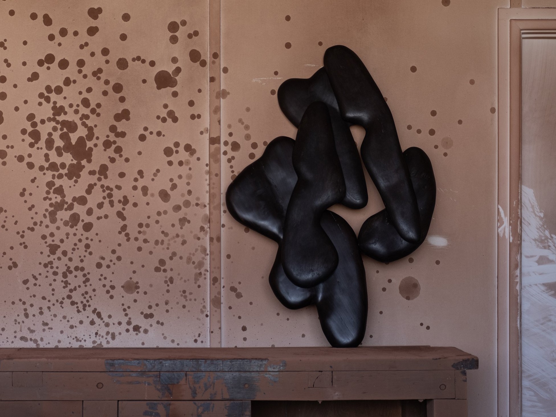 A flat sculpture leaning against the wall of the studio, made up on interlinked carved shapes
