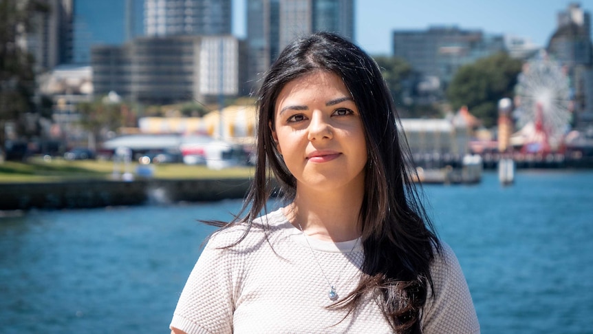 Jessica Otya, a young woman with dark hair stands by Sydney harbour.