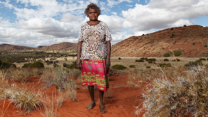 Aboriginal woman and artist Atipalku Intjalki stands in a desert landscape at Ernabella