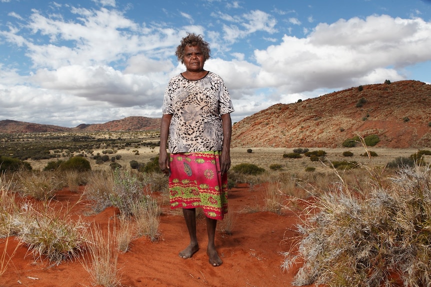 Aboriginal woman and artist Atipalku Intjalki stands in a desert landscape at Ernabella