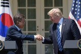 President Donald Trump and South Korean President Moon Jae-in smile as they shake hands at a White House podium.
