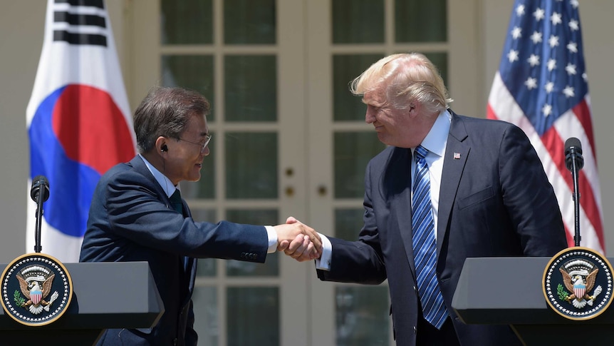 President Donald Trump and South Korean President Moon Jae-in smile as they shake hands at a White House podium.