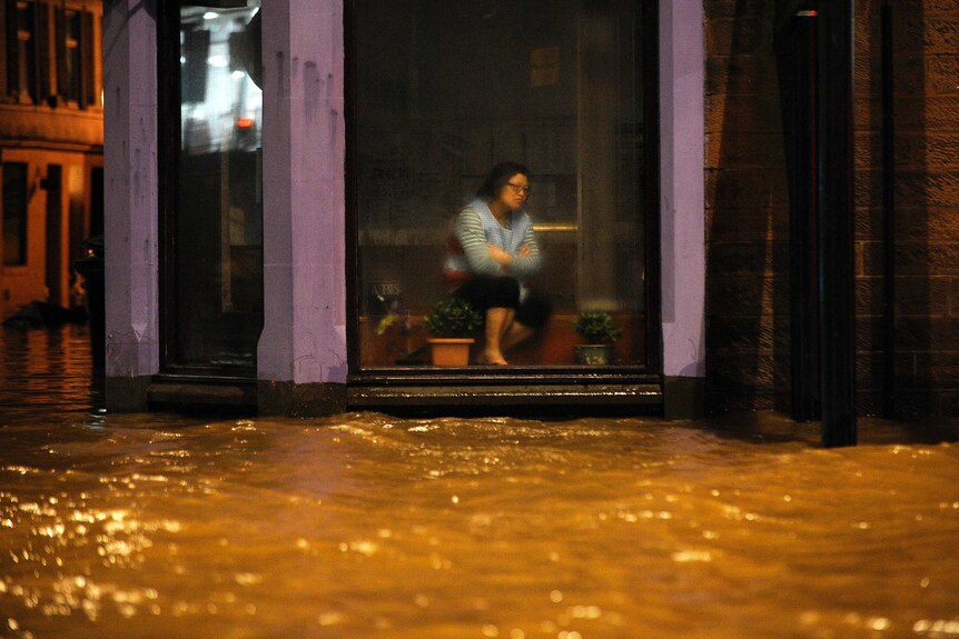 Night photo of a woman sitting inside a Chinese Restaurant watching floodwater race past.