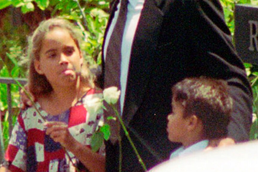 A blurry, zoomed in photo of OJ Simpson with his daughter Sydney and son Justin, who are holding roses