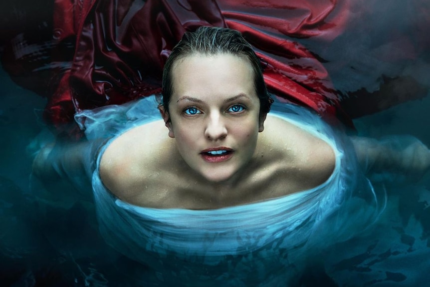 A woman dressed in blue sits in black water looking at the camera.