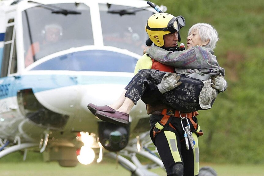 An old woman is carried to a helicopter by a rescuer.