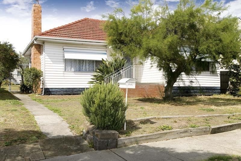 A white weatherboard house with terracotta tiled roof, orange brick chimney and large front windows, with grassy front yard.