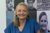 A woman smiles at the camera wearing a blue shirt. She is in an office.