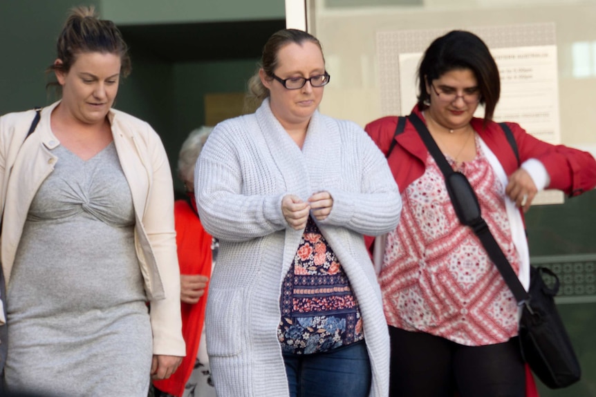 A mid shot of Nicole Martin walking from court in Perth flanked by two other women.
