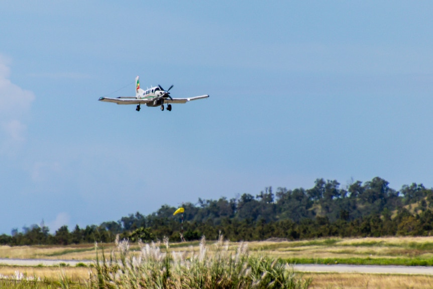 A plane hovers low in the air above a runway and trees.