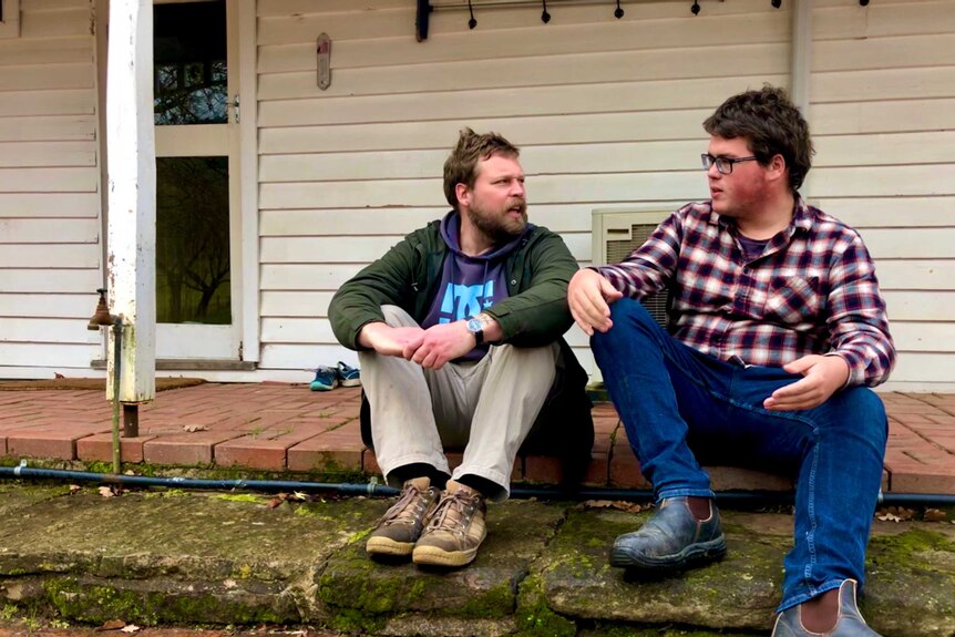 two men sit on verandah chatting
