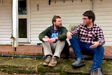 two men sit on verandah chatting