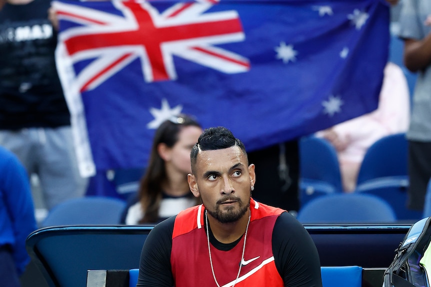 Nick Kyrgios sits with an Australian flag behind him