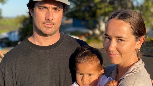 A young man and young woman and baby  look at the camera unsmiling and baby 