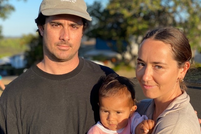 A young man and young woman and baby  look at the camera unsmiling and baby 