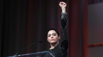 Rose McGowan stands in front of a microphone with her fist held aloft