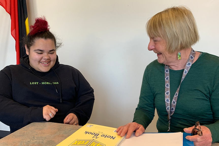 Student and teacher, both sitting at a school desk, laughing amongst themselves.