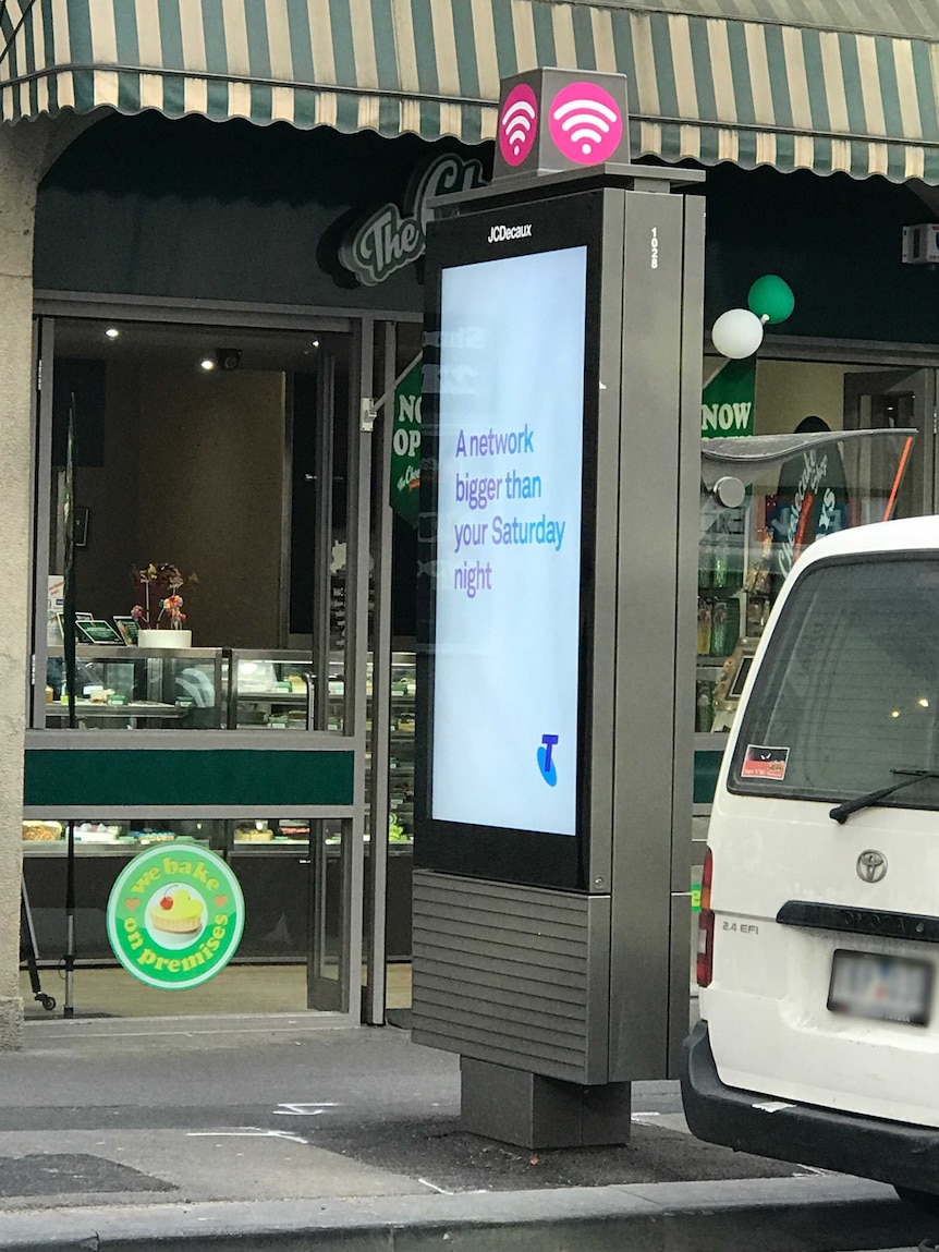 The Telstra payphone has a billboard attached to the back of it, installed in front of The Cheesecake Shop.
