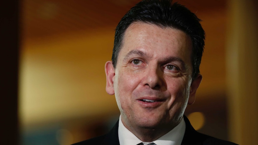 Nick Xenophon looks just off camera. Behind him, the background is blurred.