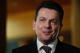 Nick Xenophon looks just off camera. Behind him, the background is blurred.