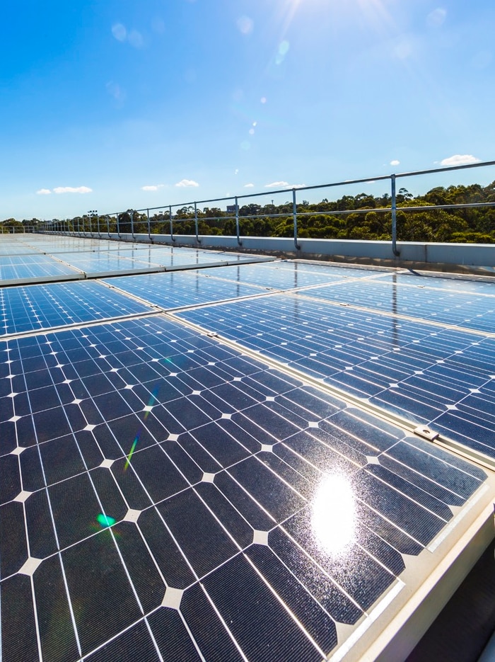 Solar panels on a roof, trees in background, sun shining and blue skies