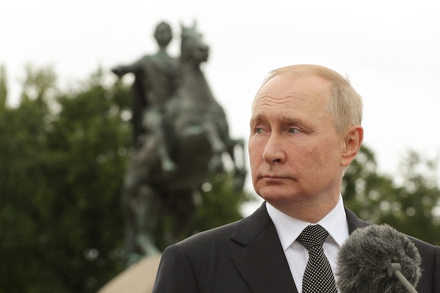 Vladimir Putin looks over his shoulder to a statue of a man riding a horse.