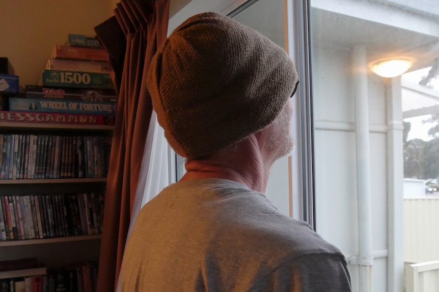 a man in a beanie looking out of a window in a house